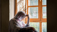 A Muslim woman next to a window, looking downwards at the outside