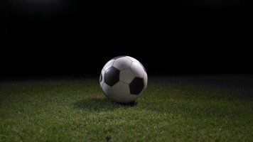 A football sitting on grass with stadium lights in the background.