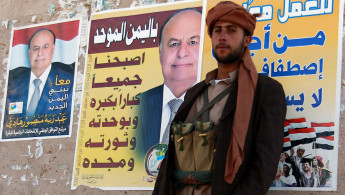 Houthi in front of Hadi poster