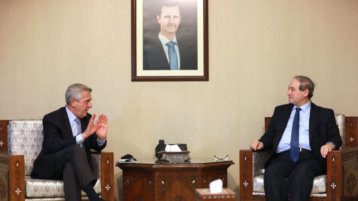 Filippo Grandi speaks with Faisal Mekdad under a portrait of dictator Bashar Al-Asasd