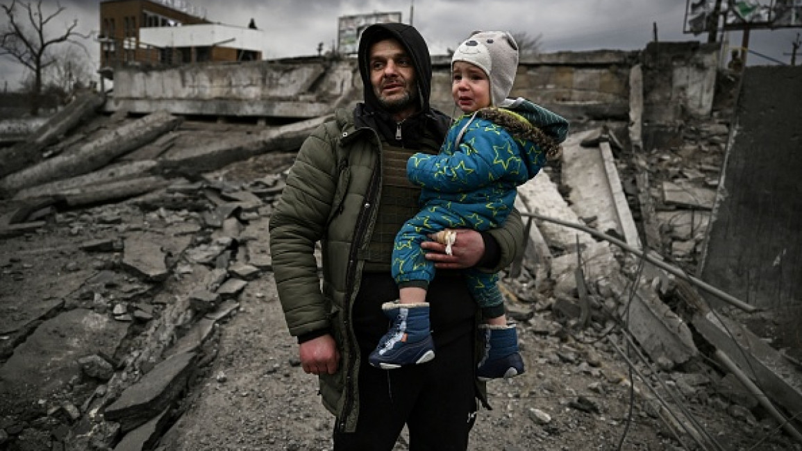 A man holding a child stands amid destruction as he flees the city of Irpin, west of Kyiv, on March 7, 2022. [Getty]