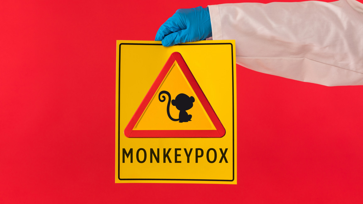 A red triangle sign with a monkey in the middle on a yellow background. Below reads the text: "Monkeypox."