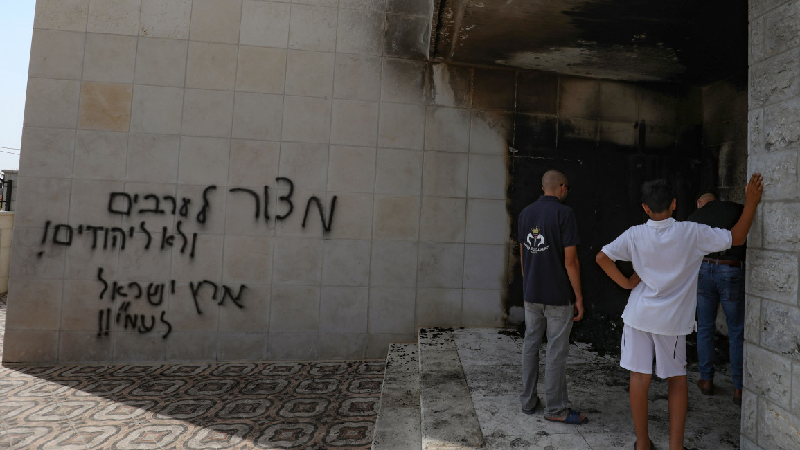 Palestinians inspect the damage at the entrance of a mosque that was torched and sprayed with graffiti in Hebrew, in Al-Bireh,