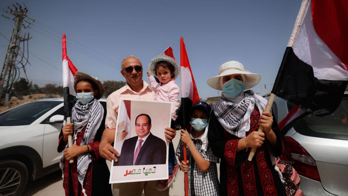 Members of a Palestinian family wave Egyptian flags and hold up a portrait of Egypt's President Abdel Fattah al-Sisi as they wait to receive the incoming Egyptian intelligence convoy