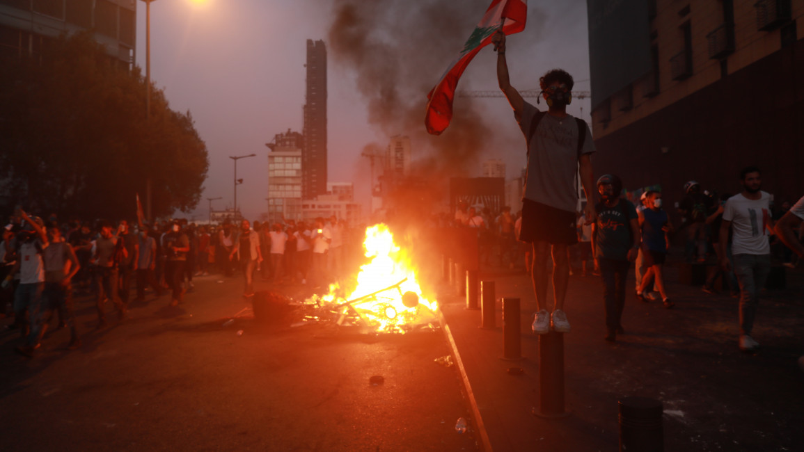 A protester waves the Lebanese flag in front of a pile of burning wood, near the Lebanese parliament building in downtown Beirut. (TNA)
