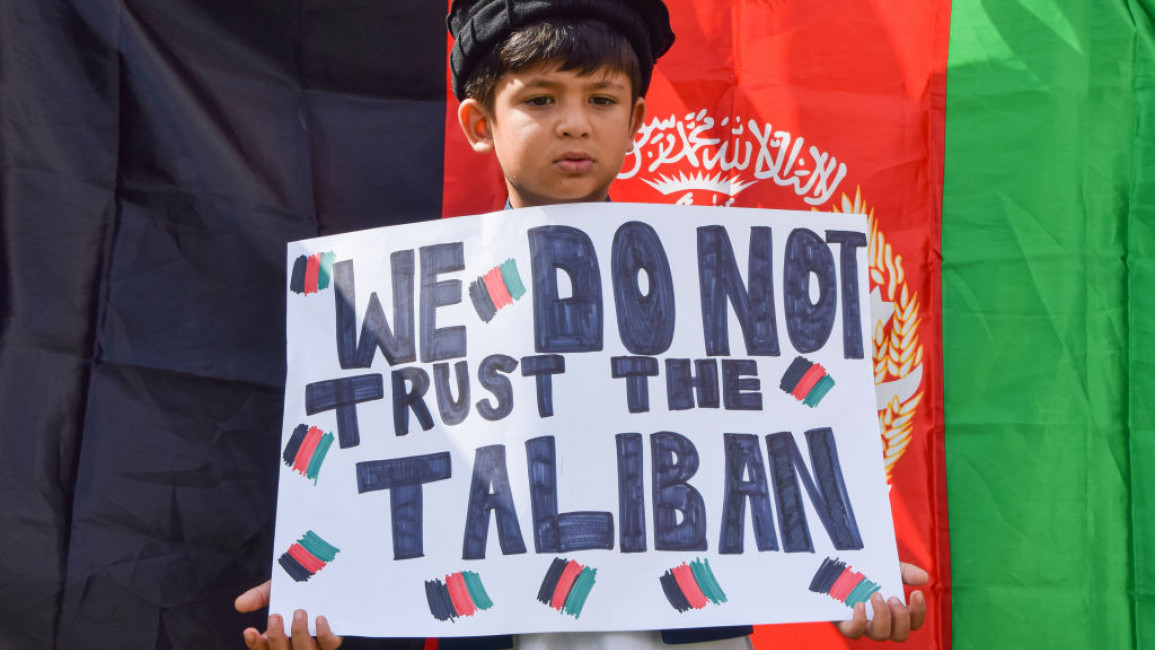 A young boy stands next to a flag of Afghanistan and holds a placard which says 'We Do Not Trust The Taliban' during the demonstration in Parliament Square. [Getty]