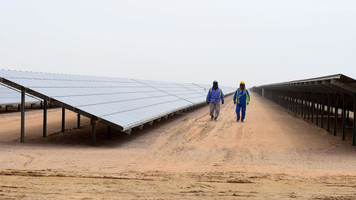 Employees walk past solar panels at the Mohammed bin Rashid Al-Maktoum Solar Park on March 20, 2017, in Dubai. Dubai completed a solar plant big enough to power 50,000 homes as part of a plan to generate three-quarters of its energy from renewables by 2050. / AFP PHOTO / STRINGER (Photo credit should read STRINGER/AFP via Getty Images)