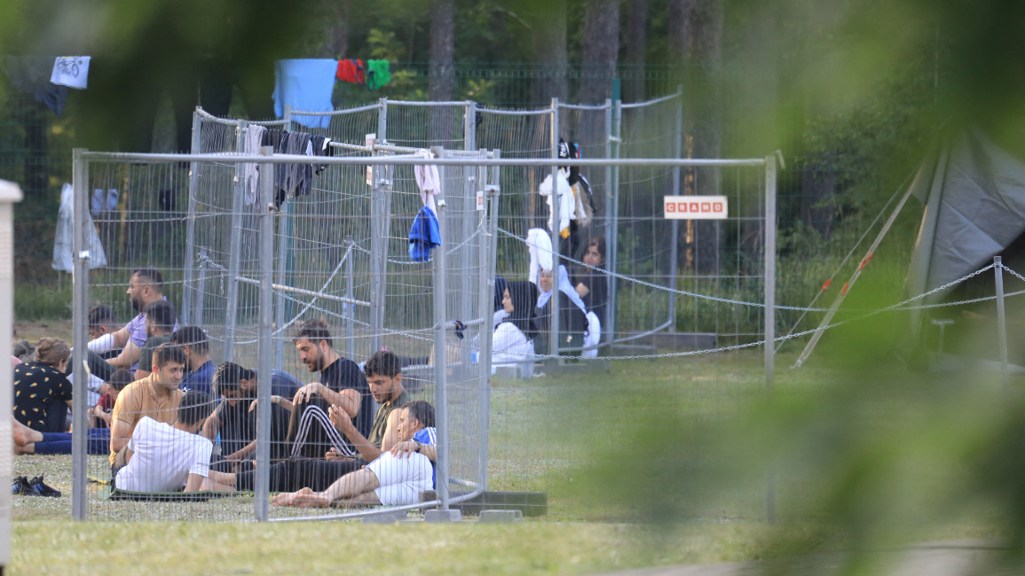 Migrants are seen through fences as they sit on the ground in a camp near the border town of Kapciamiestis, Lithuania [Getty]