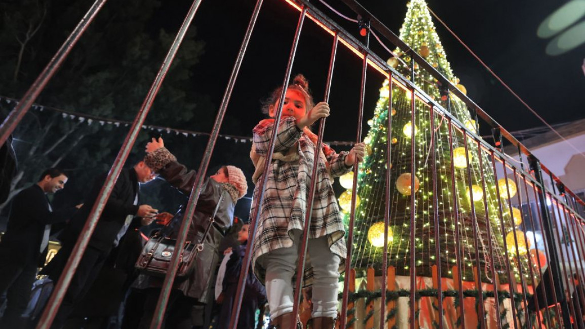 A girl holds on to a fence as she stands near the lit up Christmas tree in Gaza City