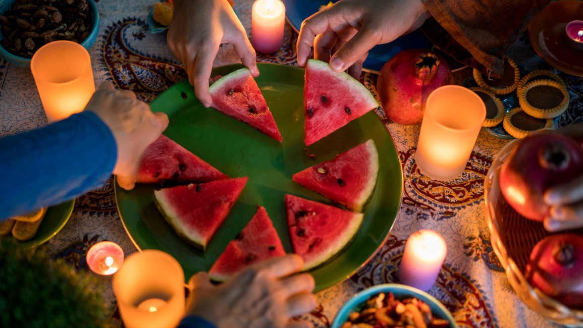 Four people taking a slice of watermelon from a plate. Candles surround the plate