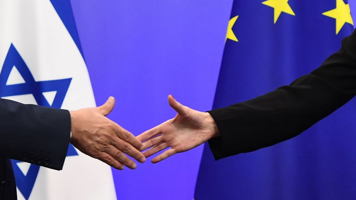 Two people shake hands as an Israeli and EU flag are in the background