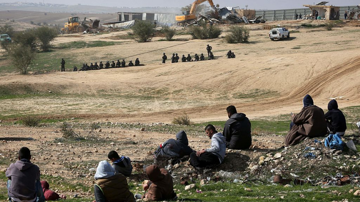 Palestinians in the Negev look on at Israeli police officers and bulldozers