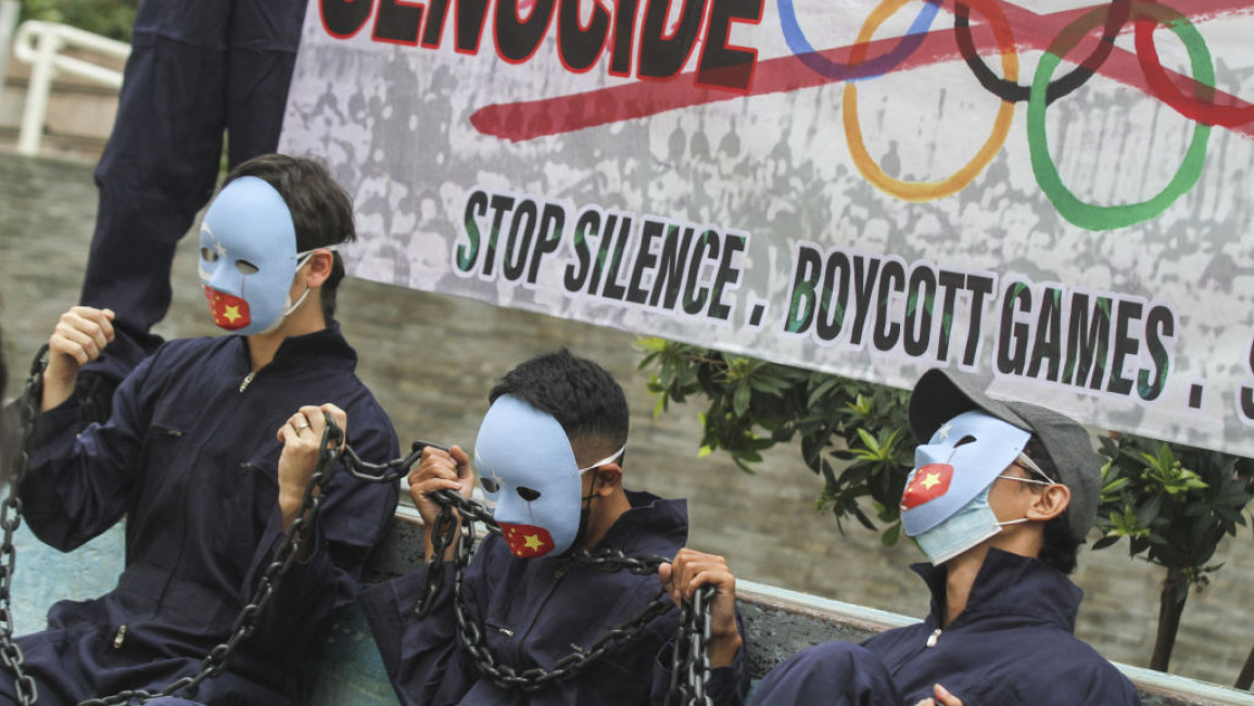 Three activists with blue masks sitting in front of a banner urging a boycott of the 2022 Olympics in China