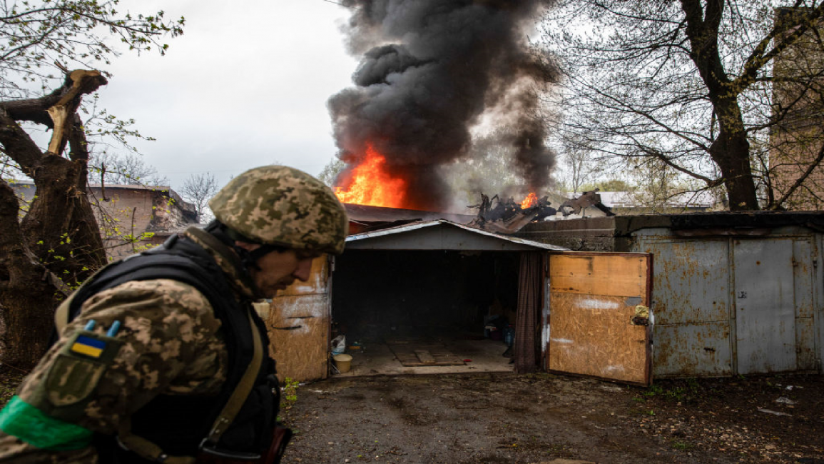 Ukrainian soldier walks past burning house