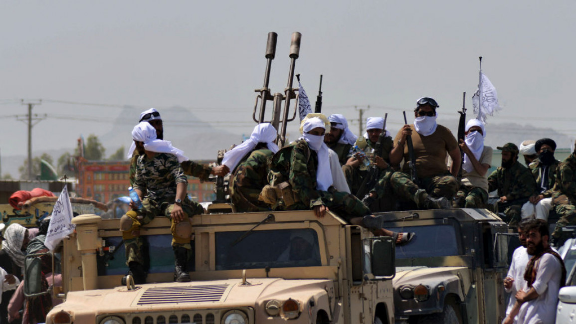 Taliban fighters wearing white face coverings sit on top of Humvees