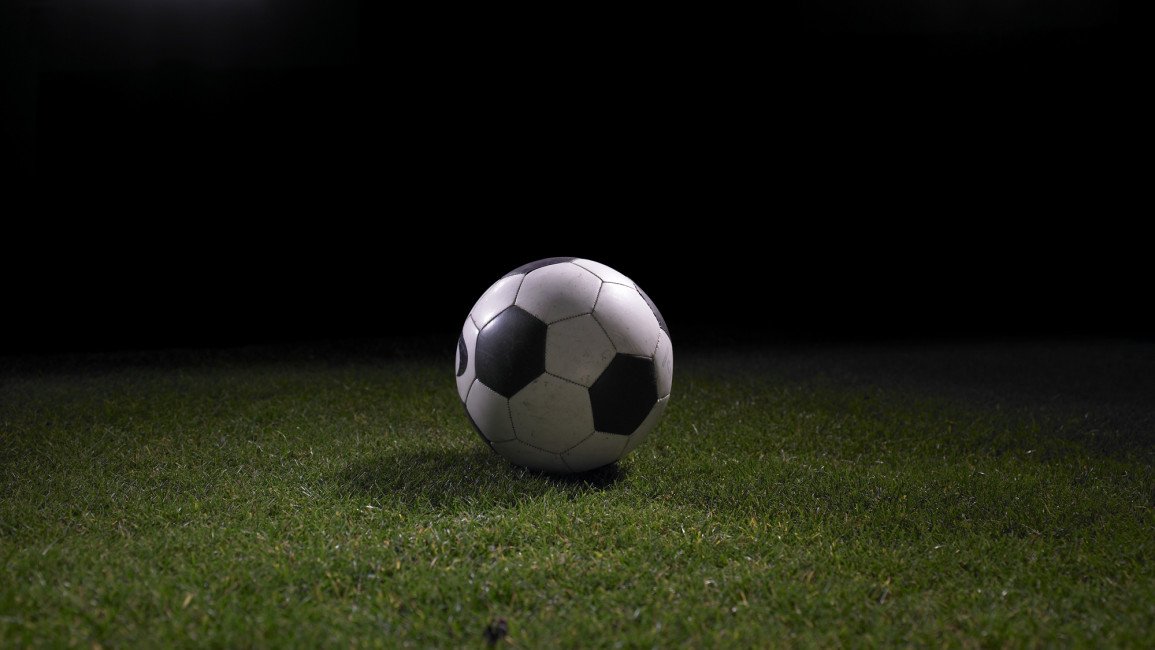 A football sitting on grass with stadium lights in the background.