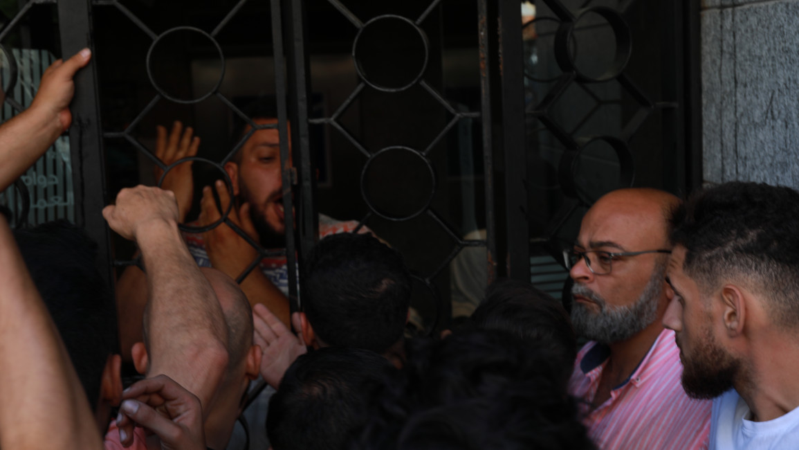 Men stand in front of a Blom Bank in Beirut as a man holds up the bank to liberate his savings. (TNA - William Christou)
