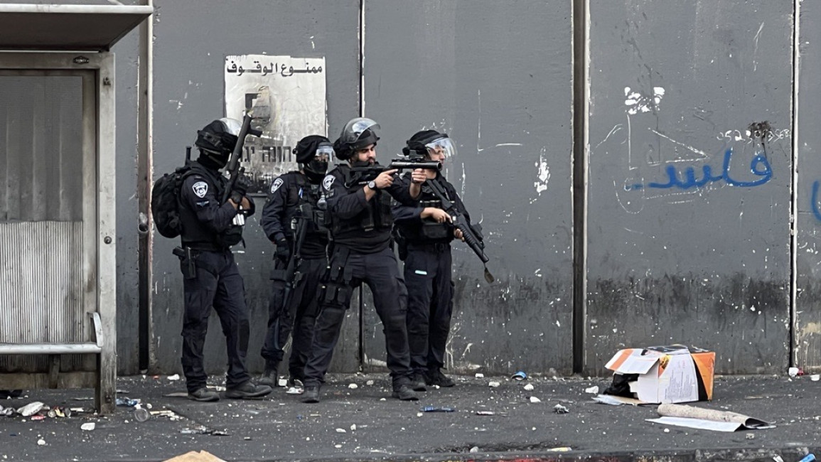Israeli policeman aims weapon at Palestinian protesters inside the Shuafat refugee camp, on 12 October 2022. [Ibrahim Husseini/TNA]