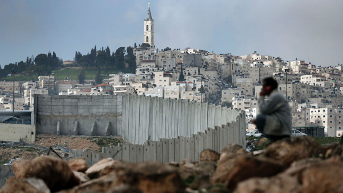 Palestinian man sits near Israel's separation barrier [AFP]