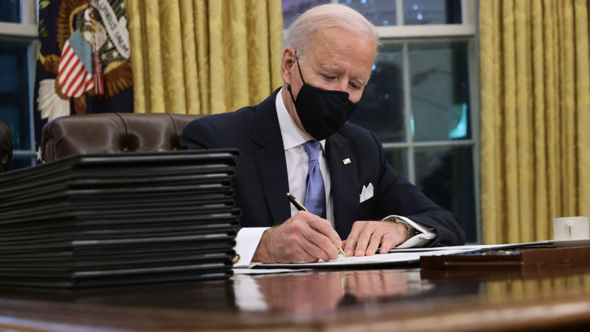 Biden signs paper in Oval Office [Getty]