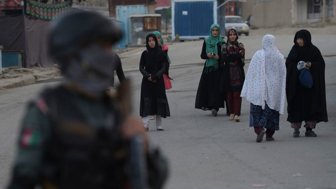 An Afghan policeman stands guard as Hazara women walk