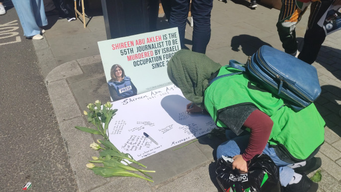 A protester writing a message on a memorial board set up to commemorate Shireen Abu Akleh
